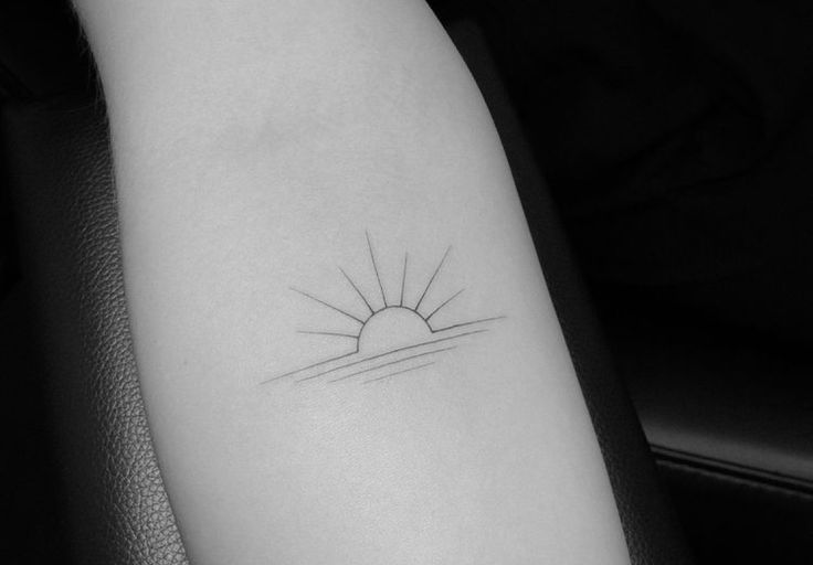 a black and white photo of a small sun tattoo on the left inner arm,