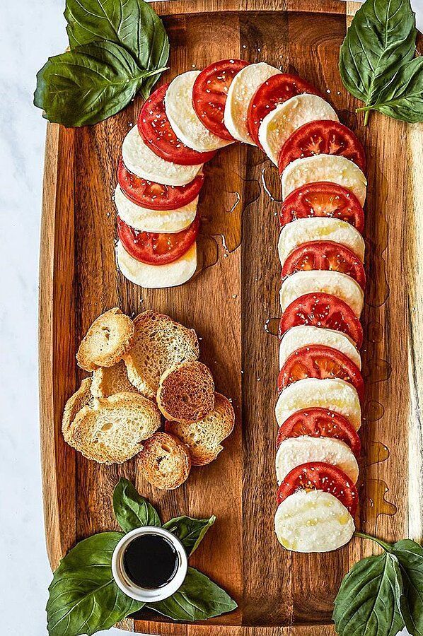 sliced tomatoes and bread on a wooden cutting board with basil leaves around the edges, next to a small bowl of dipping sauce