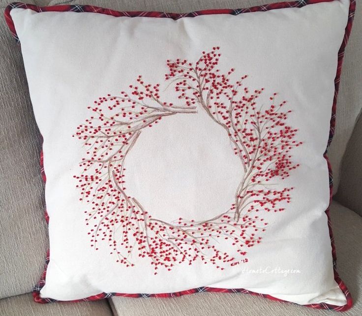 a white pillow with red berries on it sitting on top of a couch next to a chair