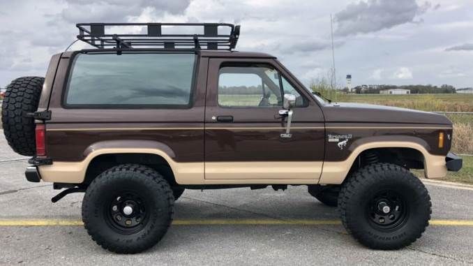 a brown and tan truck parked on top of a parking lot next to a field