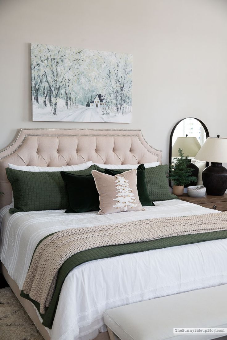 a white bed with green and beige pillows in a bedroom next to a painting on the wall