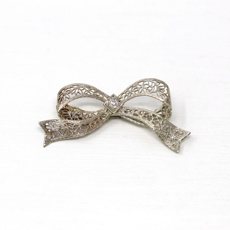 Gorgeous vintage circa 1930s era 14k white gold diamond bow brooch! This beautiful piece showcases a sparkly old European cut diamond center weighing an estimated .07 carats. The setting features ornate flower filigree with milgrain details. The brooch secures with a rotating c-clasp. An outstanding Art Deco Era piece of fine jewelry! *Sale - price reduced from $340 USD to $330 USD.  ERA - Circa 1930s - Art Deco  METAL / MATERIAL - 14k white gold, 1 old European cut diamond (estimated .07 cts, SI2, near colorless)  MARKINGS / HISTORY - Brooch clasp marked "14k"  CONDITION - Good antique condition. White gold metal has been professionally polished & cleaned. Very light age appropriate patina & wear remains. Amazing vintage bow brooch!  SIZE / MEASUREMENTS - Brooch: 1 1/2 x 3/4 inches, Weigh Platinum Brooch Jewelry As A Gift, Elegant Silver Platinum Brooches, Diamond Filigree Brooches As Gift, Vintage Engraved Brooches For Anniversary, Silver Wedding Jewelry With Decorative Bow, Silver Jewelry With Decorative Bow For Wedding, Vintage Diamond Brooches With Filigree, Vintage Platinum Brooches With Diamond Accents, Silver Bow Brooch For Wedding