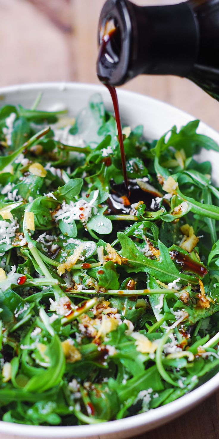 a bowl filled with greens and dressing being poured into the salad in a wine bottle