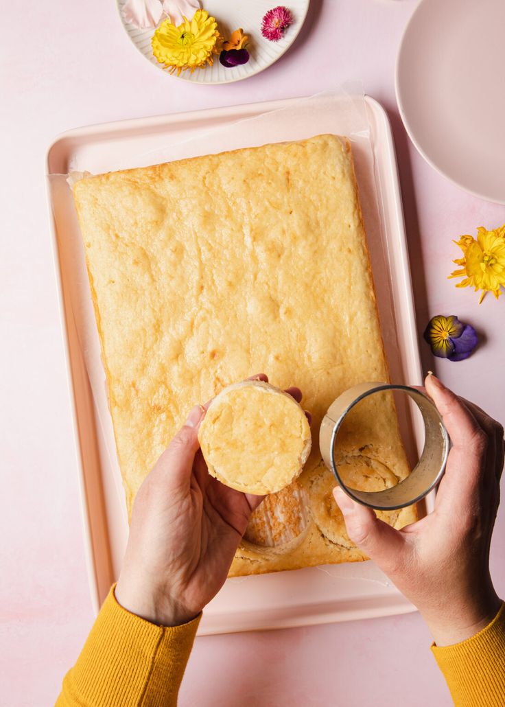 a person holding a cup in front of a cake on a plate with flowers and plates around it