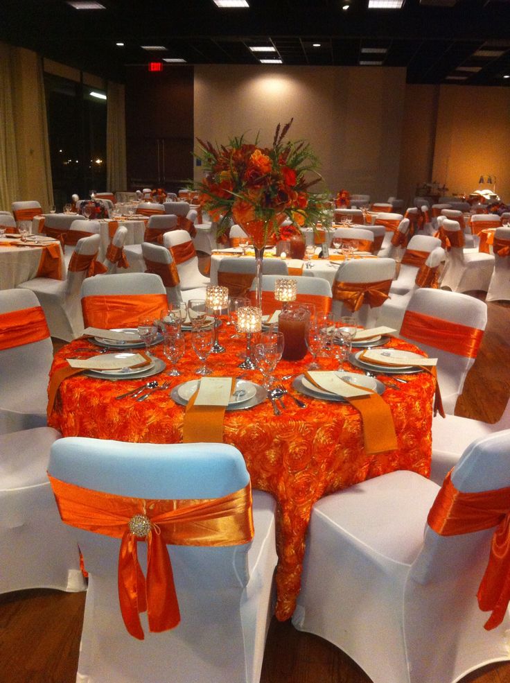 a banquet room set up with orange and white linens, place settings and centerpieces