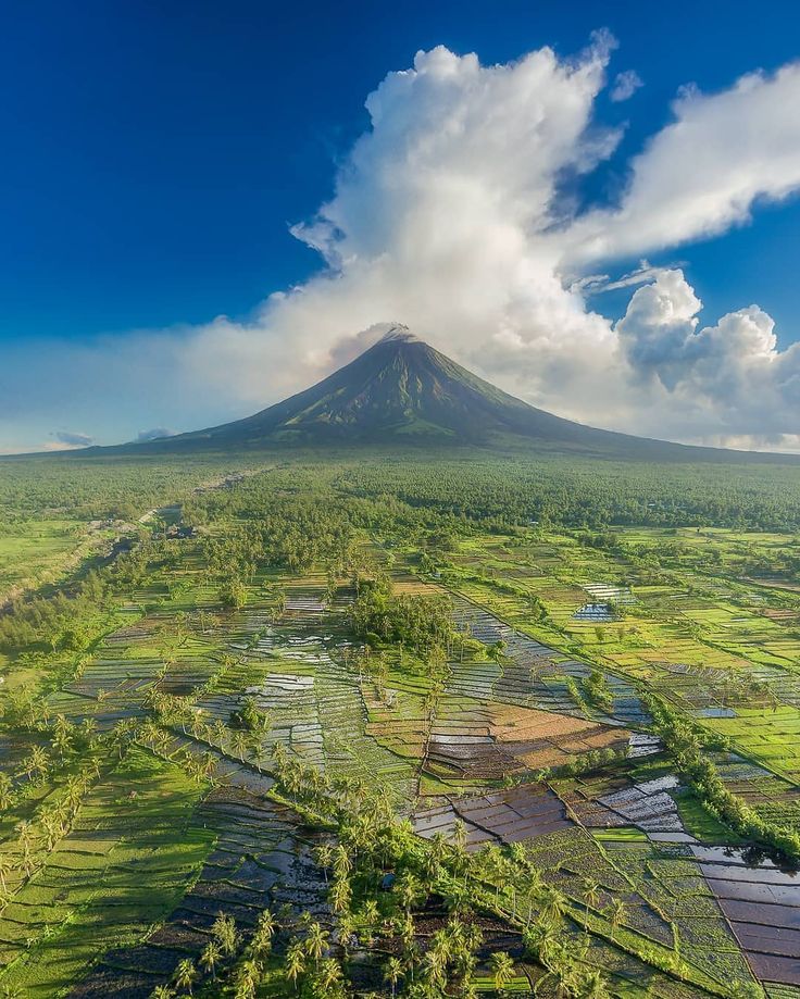 an aerial view of a mountain with rice fields in the foreground and clouds in the background