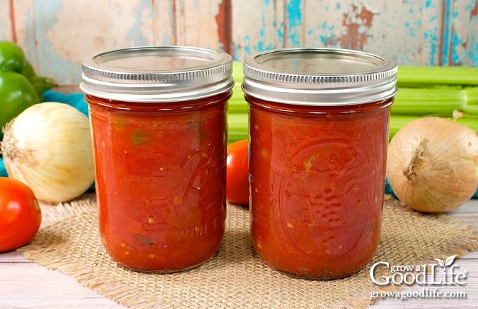 two jars filled with tomato sauce sitting on top of a table next to some vegetables