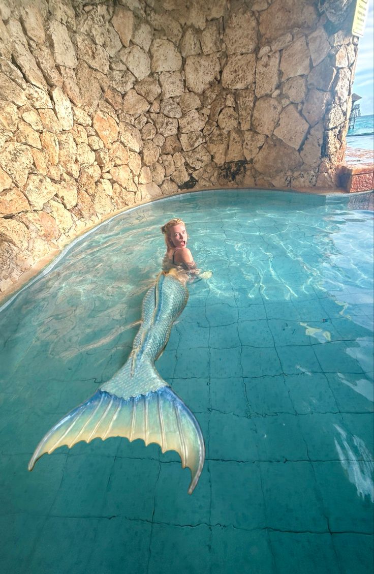 a mermaid swimming in a pool next to a stone wall