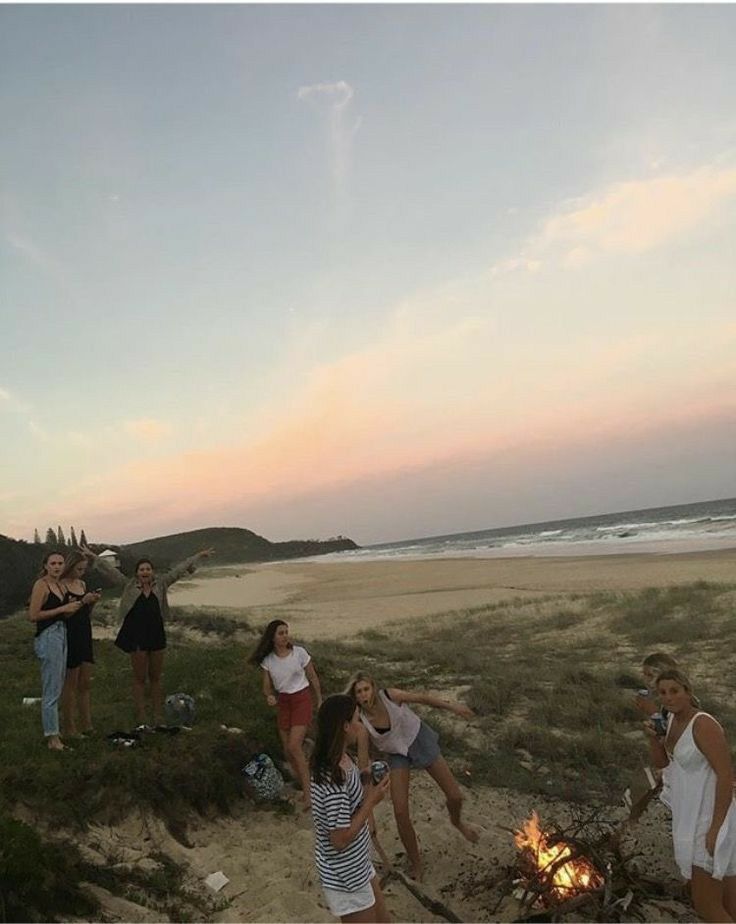 several people standing around a campfire on the beach