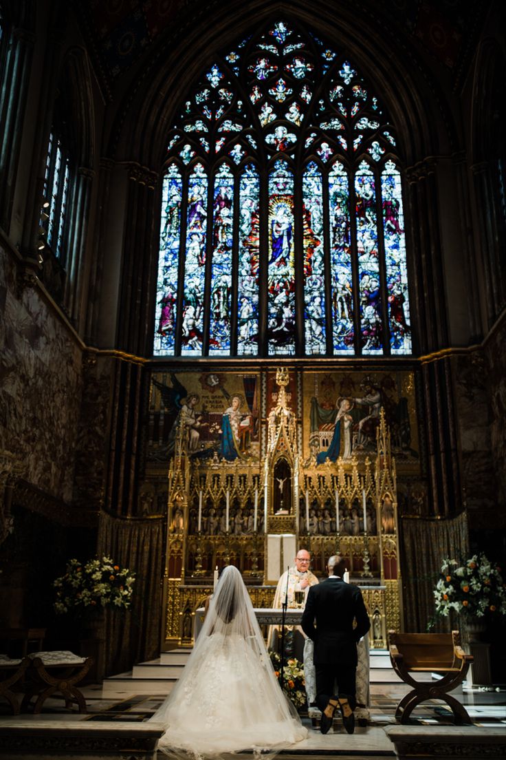 the bride and groom are standing at the alter in front of the stained glass window