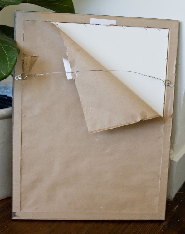 a piece of brown paper is taped to the side of a cardboard box with a plant in the background