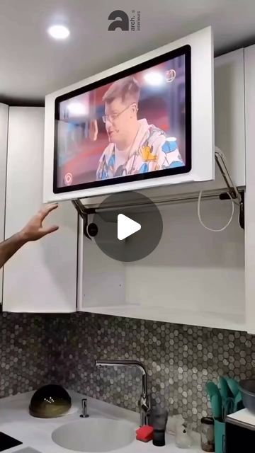 a man is pointing at a tv on the wall above his kitchen sink and counter