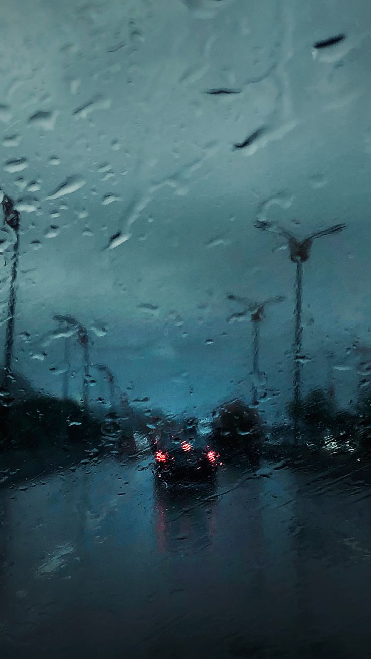 rain is pouring down on the windshield of a car and windmills in the background