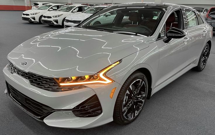 the front end of a white car in a showroom with other cars behind it