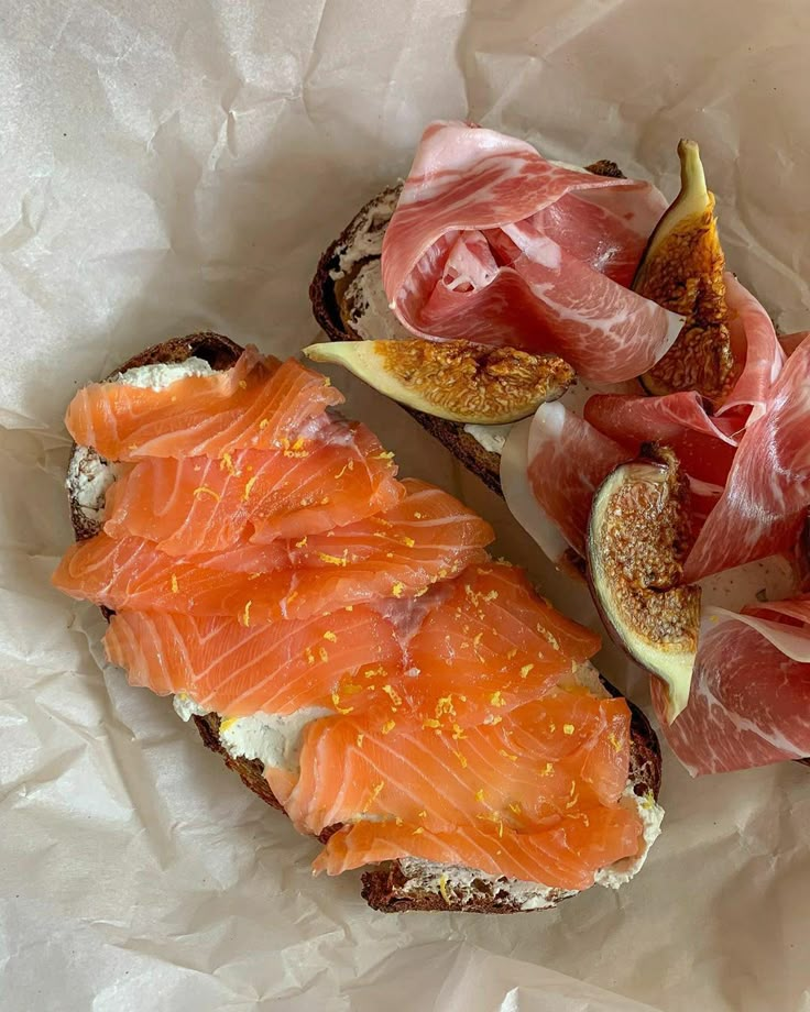 two pieces of bread with meat and cheese on them, sitting next to figs