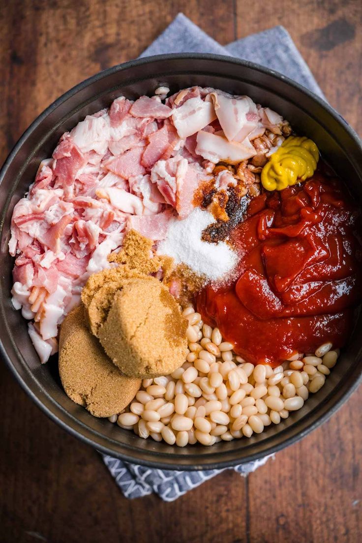 a bowl filled with beans, meat and seasoning on top of a wooden table