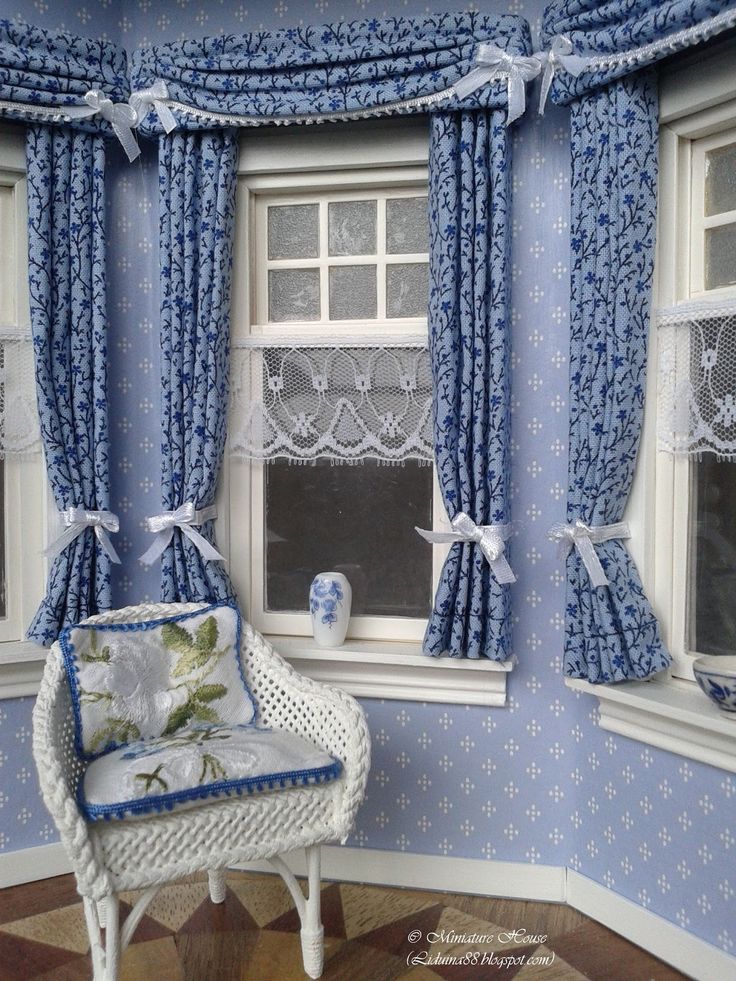 a blue and white room with curtains, windows, and a chair in front of the window