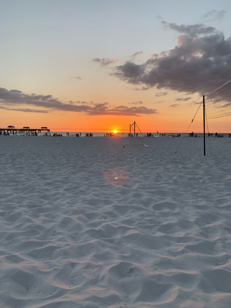 the sun is setting at the beach with volleyball nets in the sand