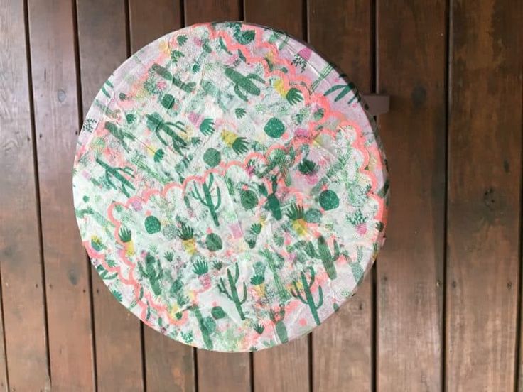 a paper plate with cactus designs on it hanging from a wooden wall in front of a wood paneled wall