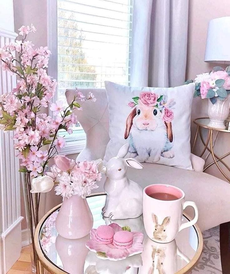 a glass table topped with pink flowers and bunny figurines next to a window