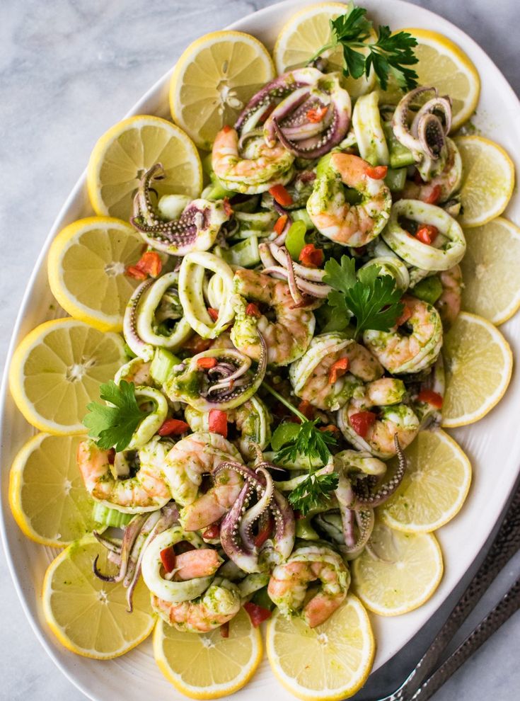 a white plate topped with lemon slices and shrimp salad next to a knife and fork