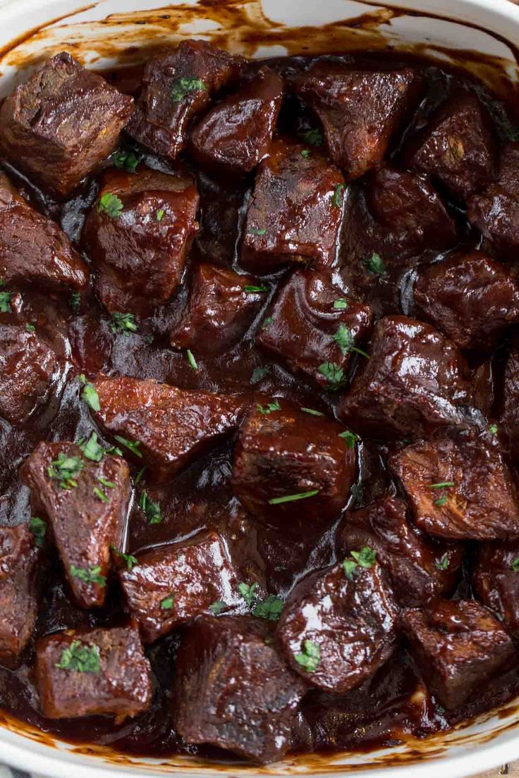 a white bowl filled with cooked beef and garnished with parsley on top