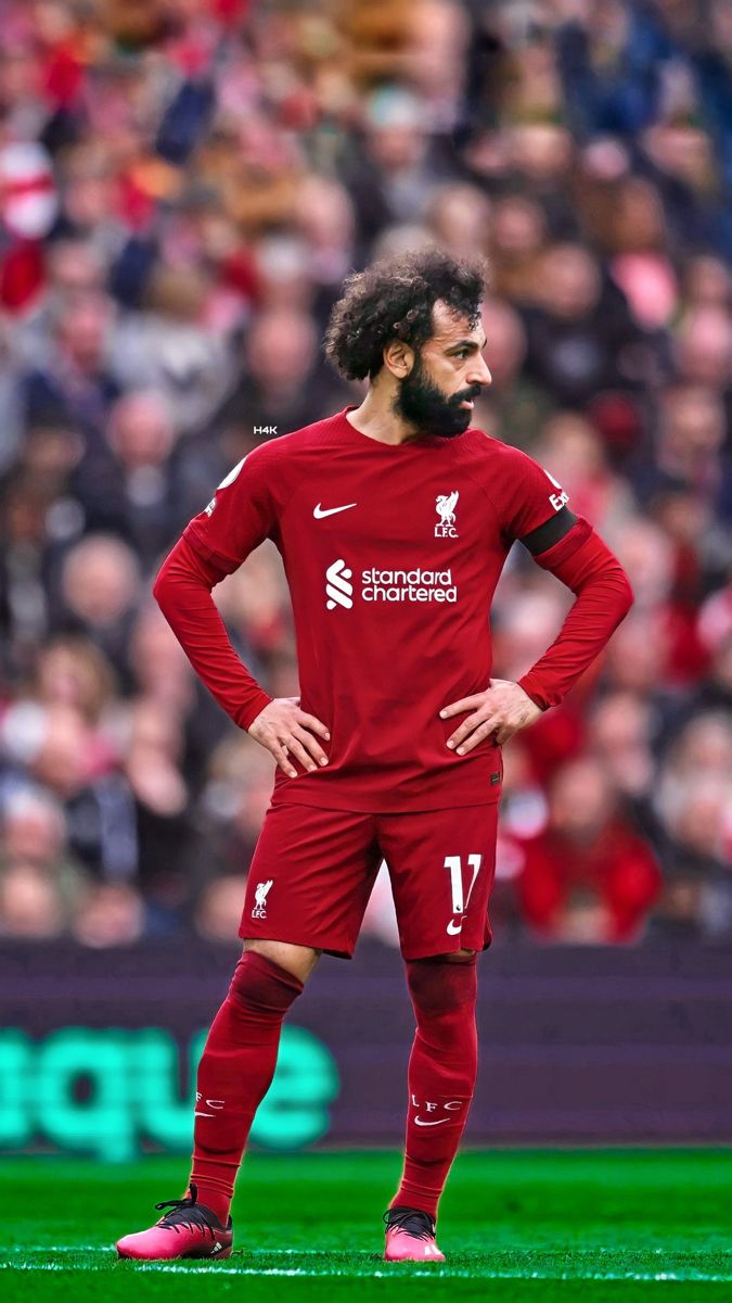 a man standing on top of a soccer field wearing a red uniform with his hands on his hips