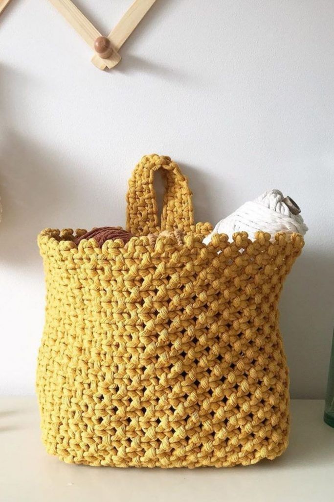 a crocheted yellow bag sitting on top of a table next to a bottle