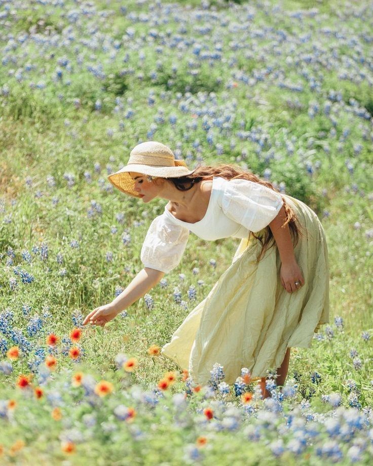 a woman picking flowers in a field with blue and orange wildflowers behind her