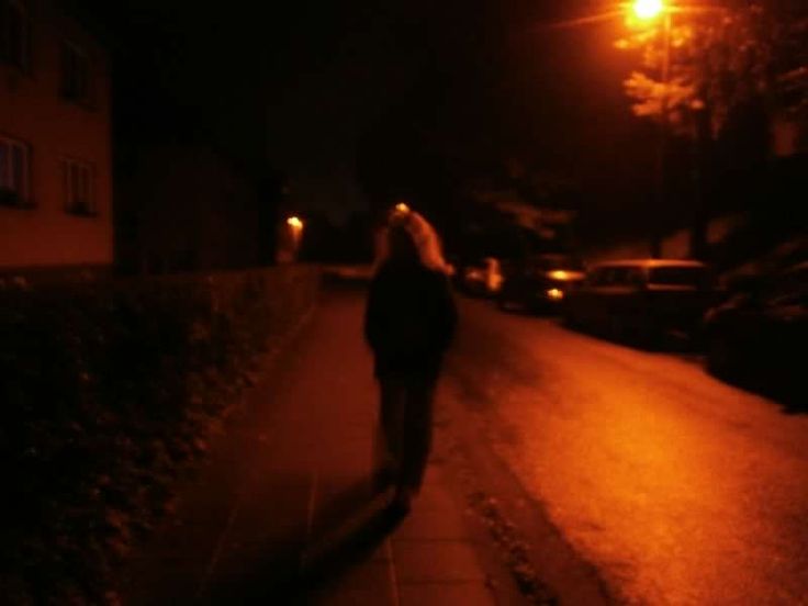 a woman is walking down the street at night with her head turned to the side