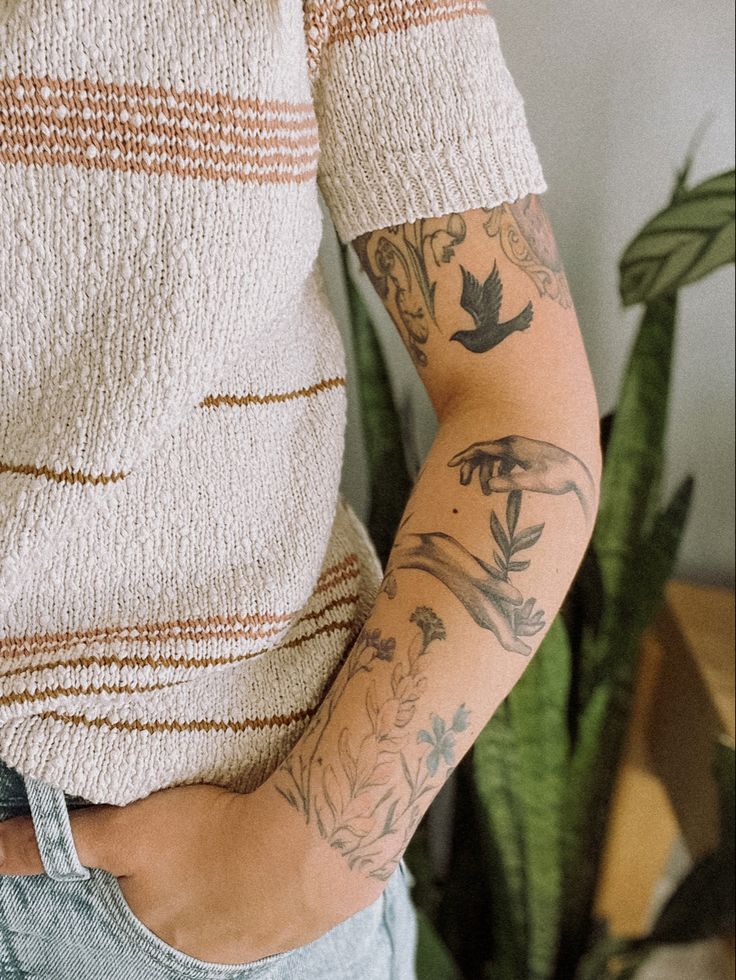 a woman with tattoos on her arms and armbands is standing in front of a potted plant