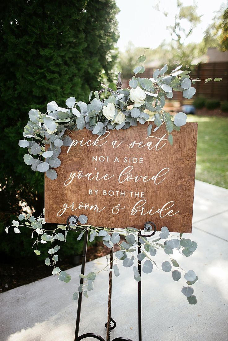 a wooden sign that has some flowers on it and is sitting in front of a tree