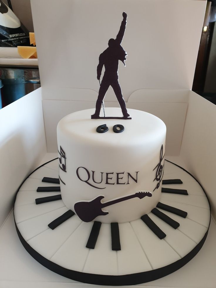 a white cake with black letters and a figure on top that reads queen, surrounded by piano keys