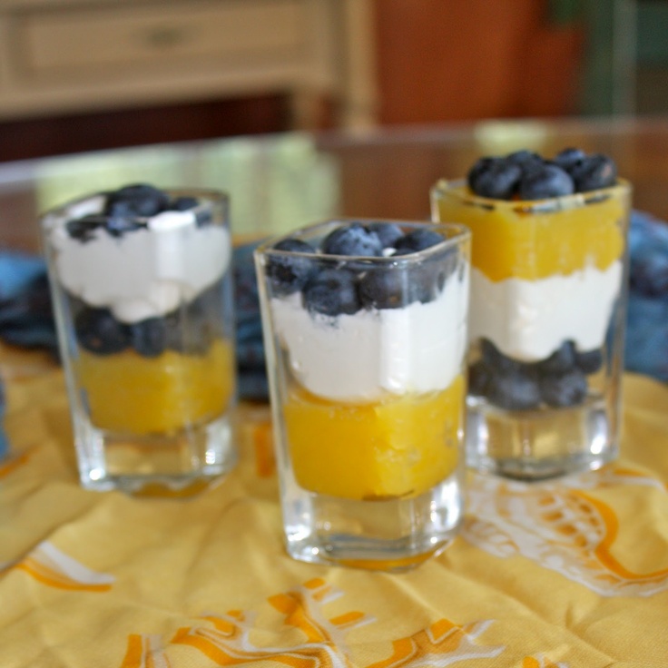 three glasses filled with dessert sitting on top of a table next to blueberries and lemons