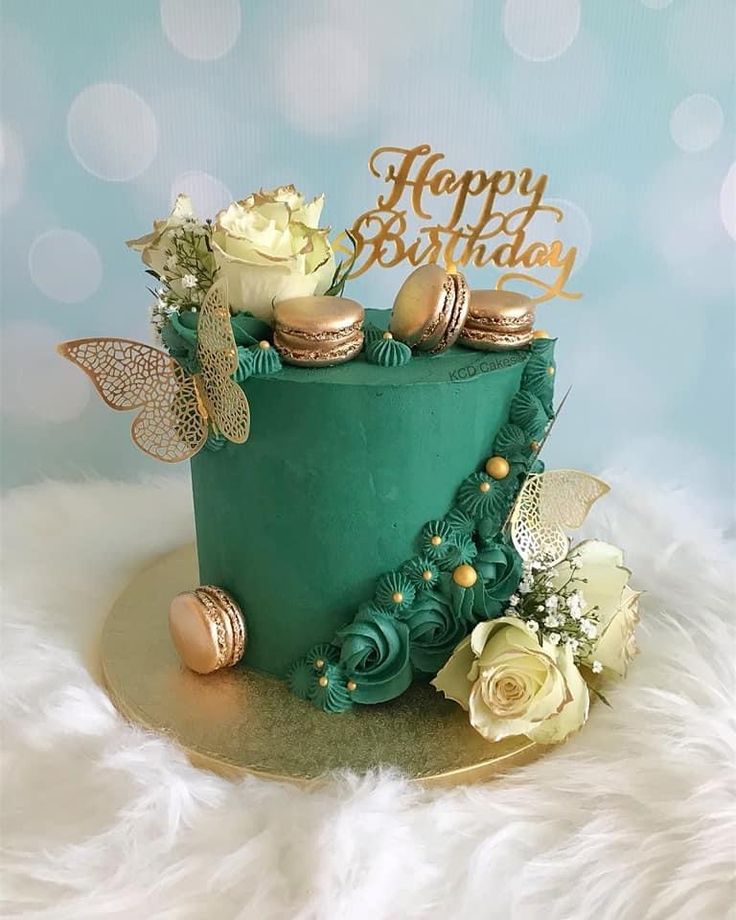 a green birthday cake with gold decorations and flowers on top, sitting on a white furnishing