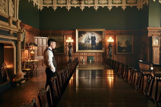 a man standing in the middle of a room with chairs and paintings on the walls