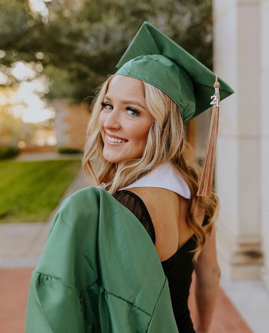 a woman wearing a green graduation gown and cap is smiling at the camera with her hands in her pockets