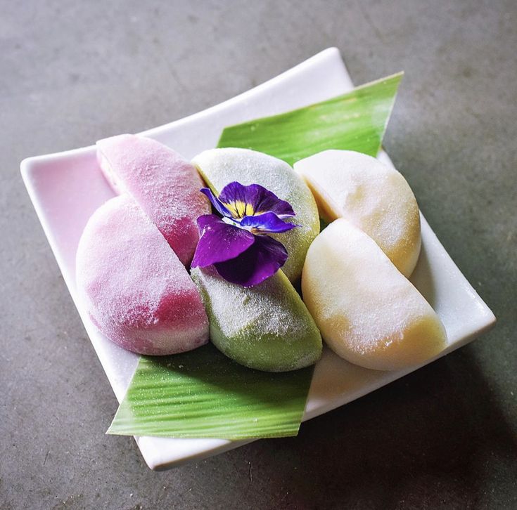 there are four different types of pastries on the plate with green leaves and purple flower