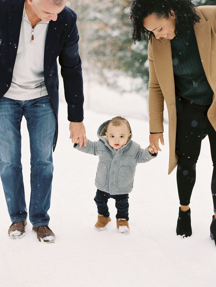 a man and woman holding hands with a small child in the snow