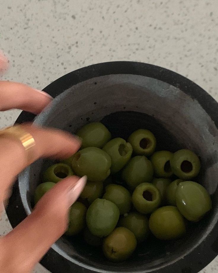 a woman's hand reaching for green olives in a bowl