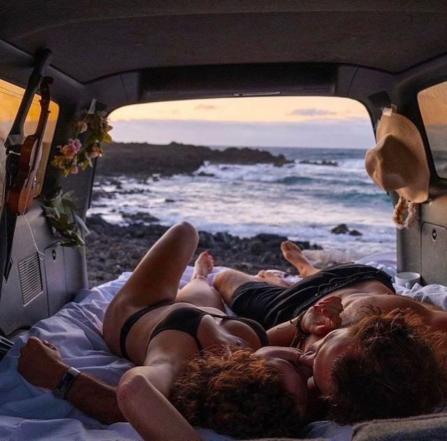 two people laying in the back of a van on top of a bed next to the ocean