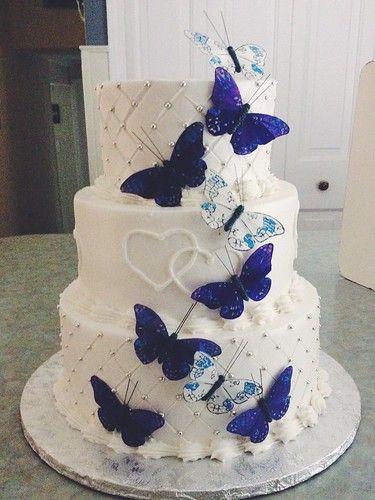 a three tiered cake with blue butterflies on the top and white frosting in the middle