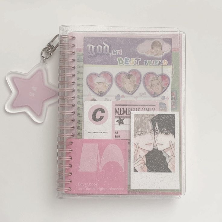 a pink notebook with various stickers and a star shaped keychain