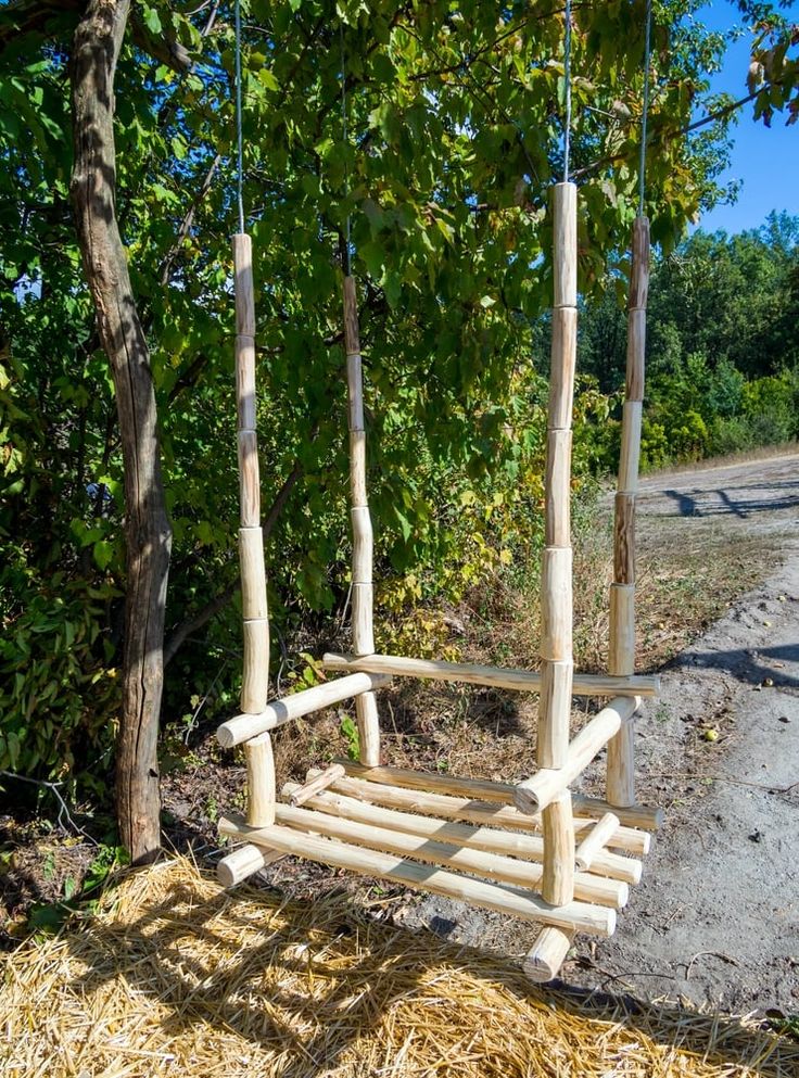 a wooden swing made out of sticks in the middle of a field next to some trees