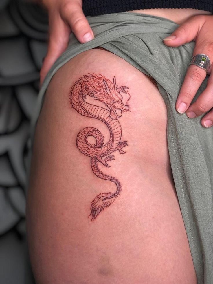 a woman with a dragon tattoo on her thigh is holding onto the side of her leg