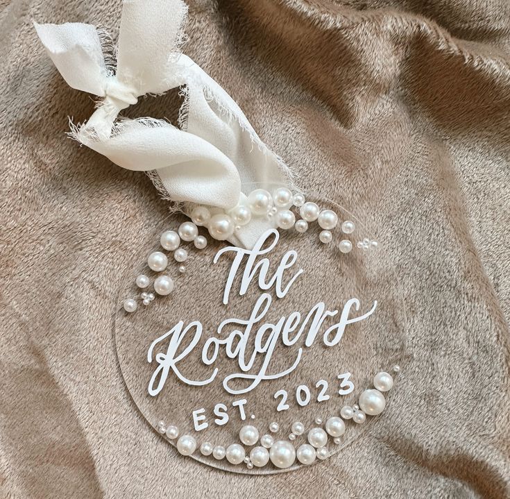 a personalized glass ornament with pearls and ribbon on a gray fabric background