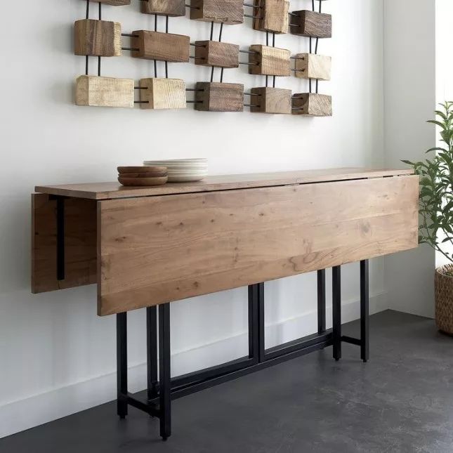 a wooden table with metal legs in front of a white wall and potted plant