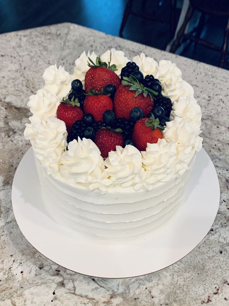 a white cake topped with strawberries and blueberries on top of a marble counter