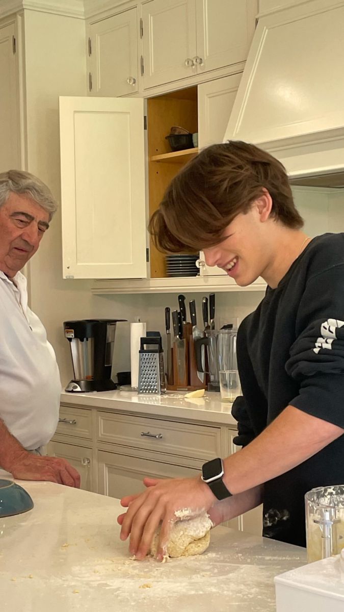 two people in a kitchen preparing food on a counter top and one person is using a cell phone