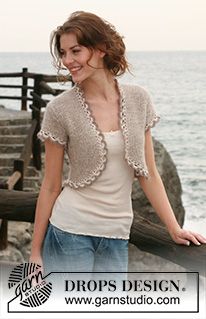 a woman standing next to the ocean with her hands in her pockets and smiling at the camera